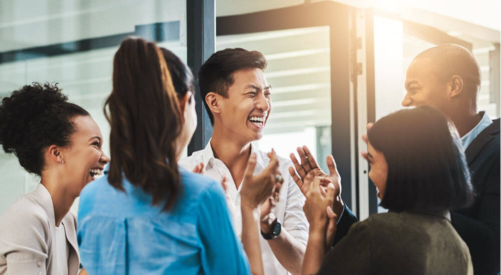 Group of young businesspeople standing together and clapping in a modern office